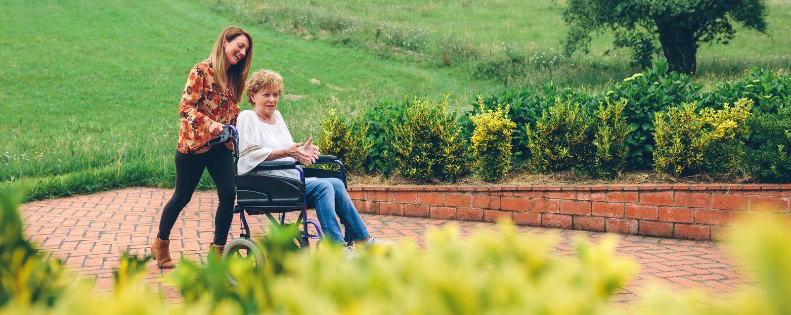 A caregiver walking a resident through the garden in her wheelchair